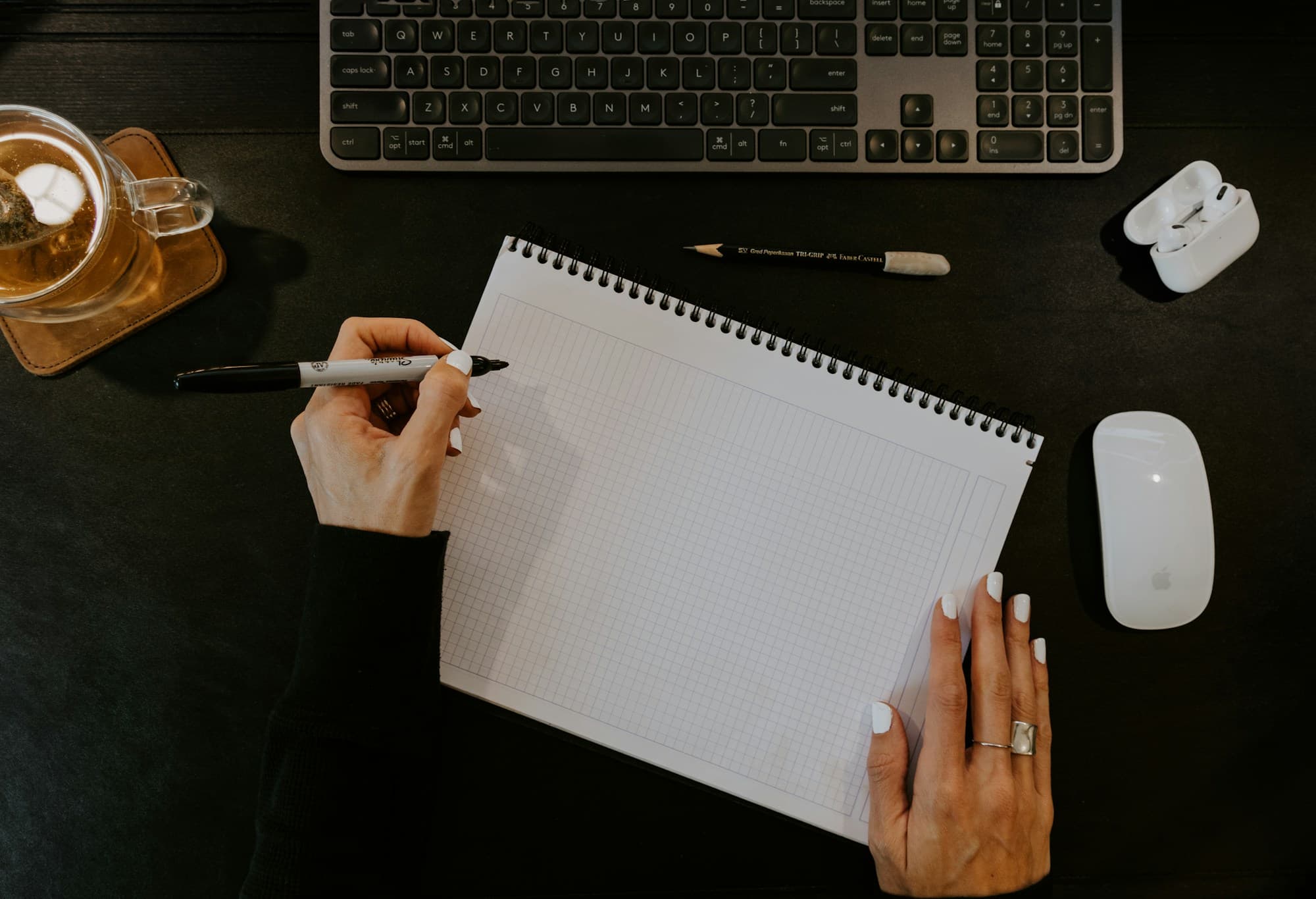 Mãos escrevendo em um caderno sobre uma mesa de trabalho